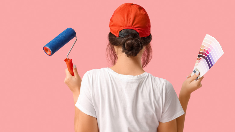 Woman facing pink wall while holding roller and samples