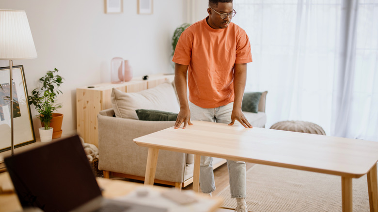 Man moving wooden table away from the window