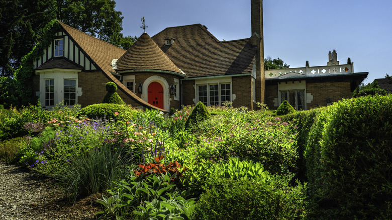 Tudor-style brick house with many bushes and shrubs planted in front.