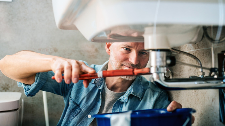 A man tightens a plumbing fixture under a sink