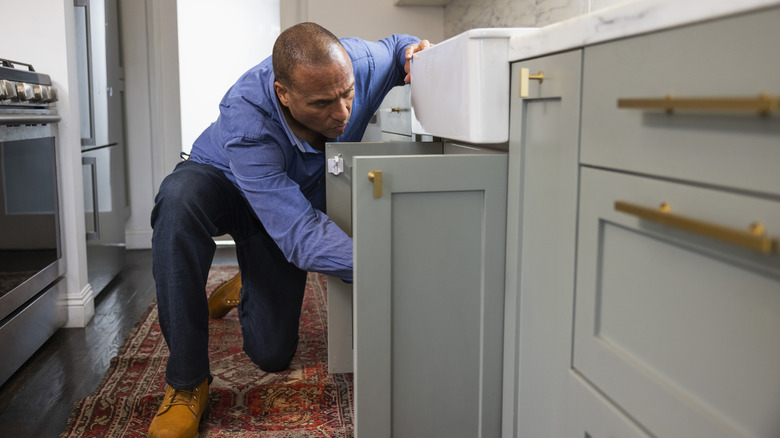 A man inspects a plumbing problem in a cabinet under a sink
