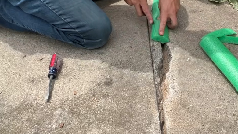 Man repairing a crack with a green pool noodle