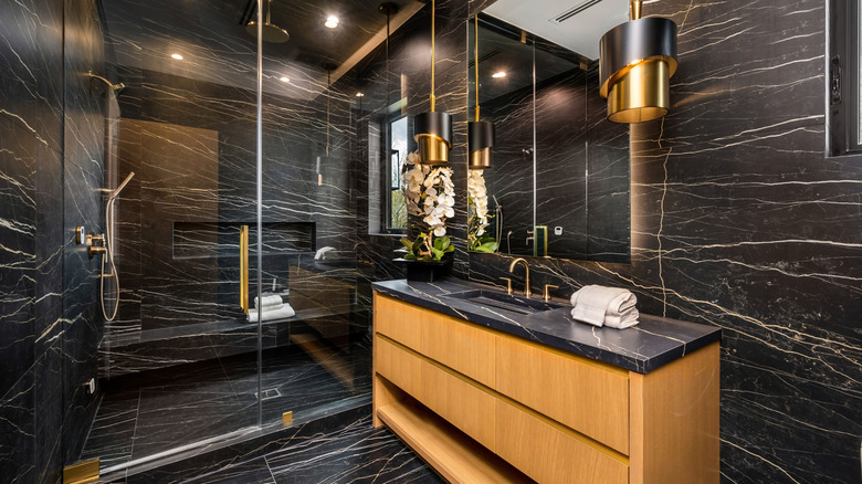 Modern bathroom with black marble on walls, floors, and counter, with wooden cabinet and gold accents