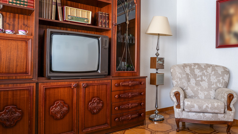 A 1980s living room with a wooden entertainment console, lamp, and chair.