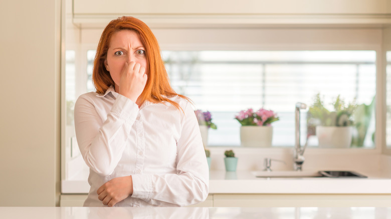 A woman holding her nose cause of bad smell in kitchen.
