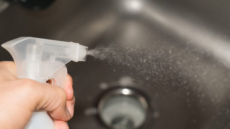 Someone spraying a clear liquid in a sink.