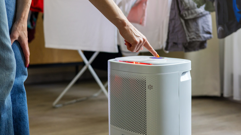 A person turning on a dehumidifier next to drying laundry