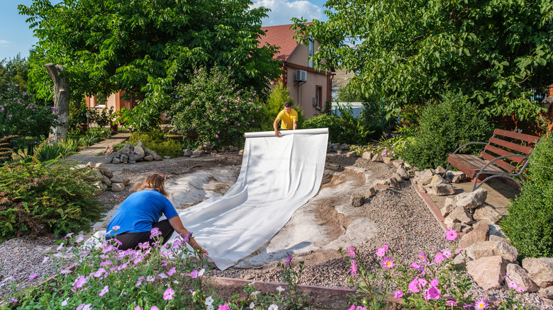 Two people laying fabric outside for a fish pond