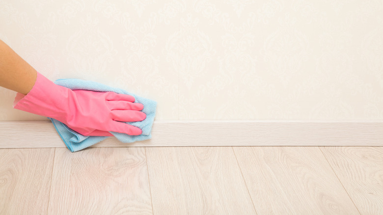 Woman cleaning baseboards with a cloth wearing a pink rubber glove