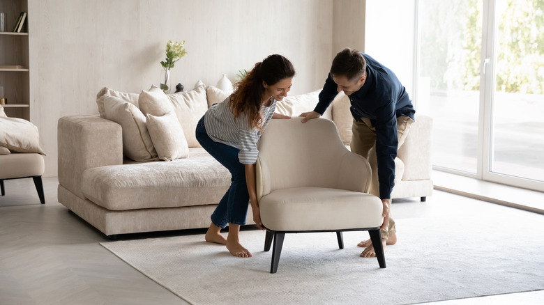 A woman and a man carrying an arm chair.