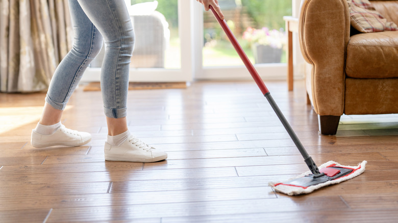 A person using a sweep and mop tool to clean their hardwood floors