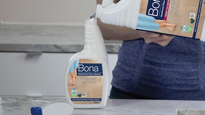 A person refilling the Bona hardwood floor cleaner spray bottle with the refill jug
