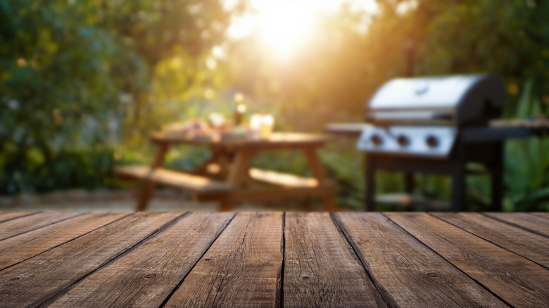 A backyard picnic table and grill are ready for an outdoor dinner.