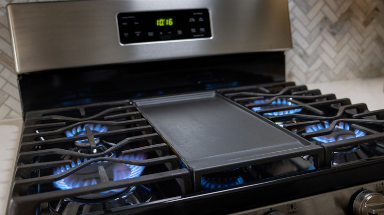 A gas stove with four lit burners and a grill pan in the center