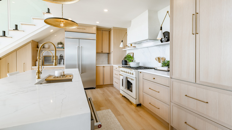 Transitional kitchen with wood cabinets, wood floors, marble island, brass hardware and lighting, and stainless steel fridge.