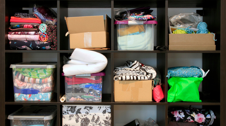 A shelf with boxes, clear bins, random clutter, and cloth containers arranged messily on the shelf