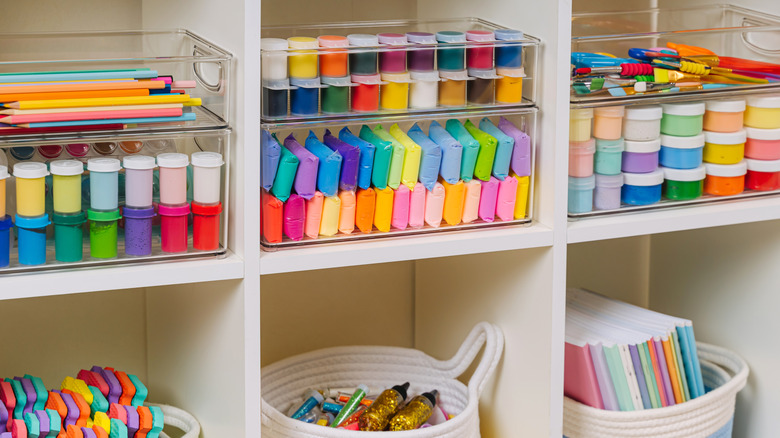Clear bins with art supplies neatly stacked including paint, clay, pens, and pencils