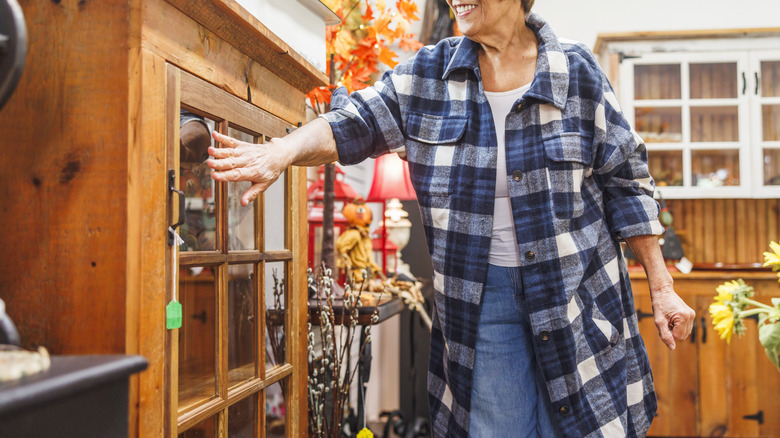 A person wearing a blue plaid shirt excitedly looks at an antique cabinet while shopping