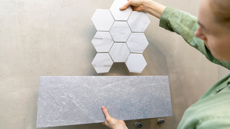 A woman holding up two styles of bathroom tile, one rectangular and one hex tile, in comparison