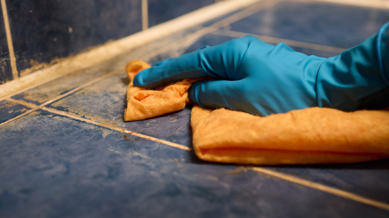gloved hand using a cloth to clean tiled surface