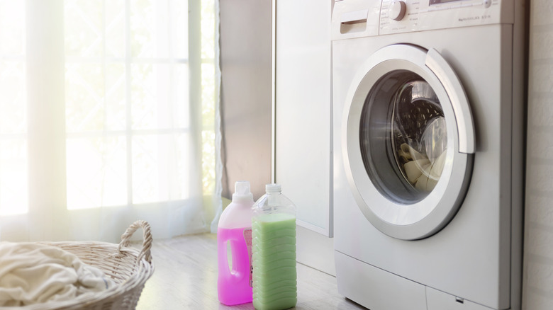 A washing machine to the right side of the image with pink and green bottled liquids in front of it