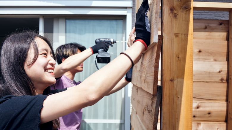 A man and woman building a wooden louvered fence