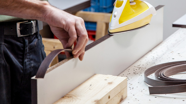 Carpenter using an iron to stick wood veneer to a piece of board