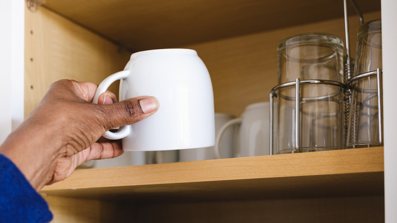 A person takes a mug out of a cabinet