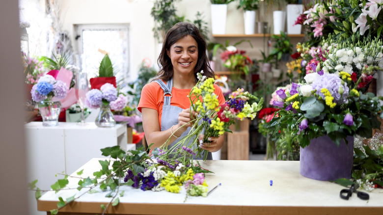 A woman smiles while putting together a bouquet of fresh flowers in a florist's shop