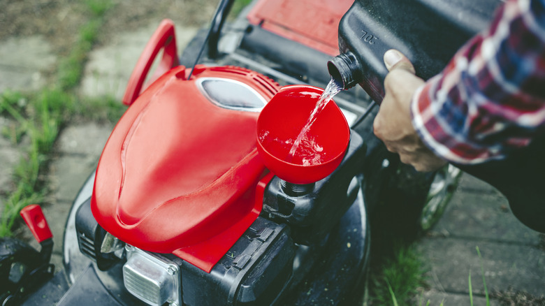 A person refilling gas on a lawn mower