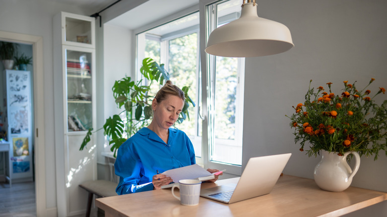A woman holding a notepad and pen researches professional houseplant repotting services on her computer.