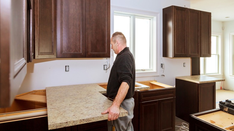 Man installing laminate countertop on dark wood kitchen cabinets