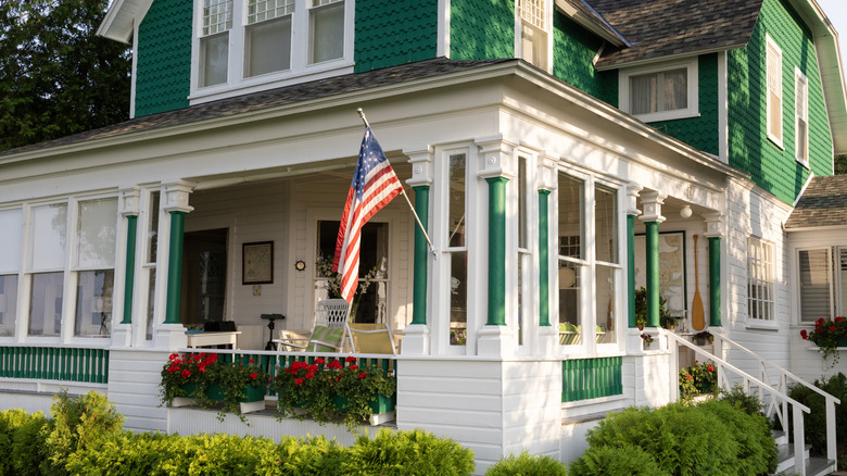 A green and white cottage with a wraparound porch.