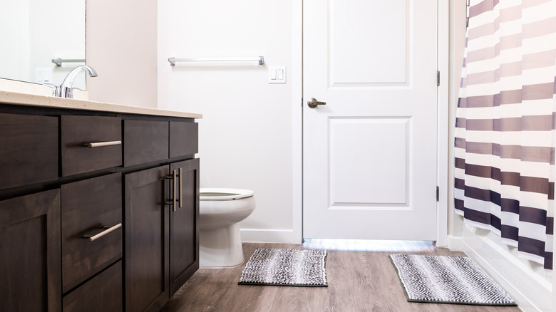 A modern bathroom with a striped shower curtain and matching rugs on the floor.