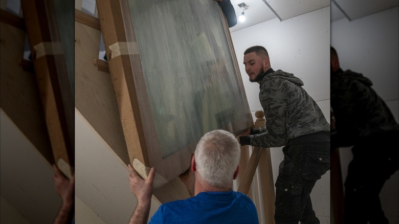 Workers carrying a window through a hallway