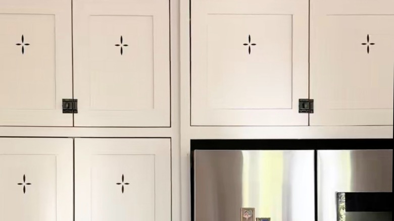 White kitchen cabinets with black stickers mimicking vents near a refrigerator