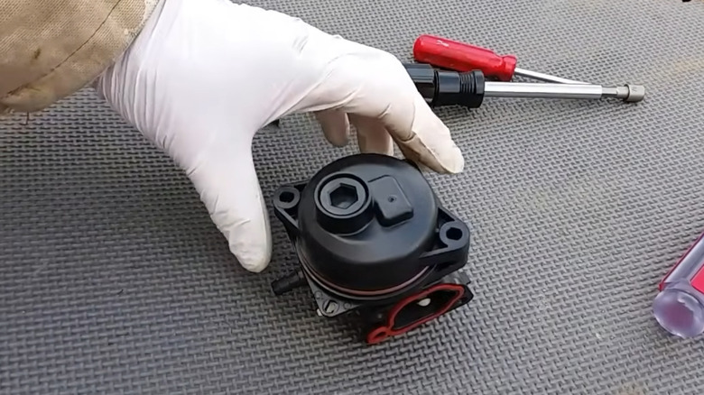 A hand grabbing a plastic small engine carburetor