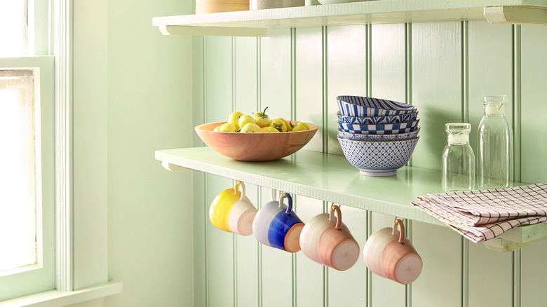 Mugs hanging from hooks beneath a kitchen shelf