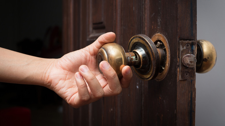 A person reaches for a doorknob that is falling off the door.