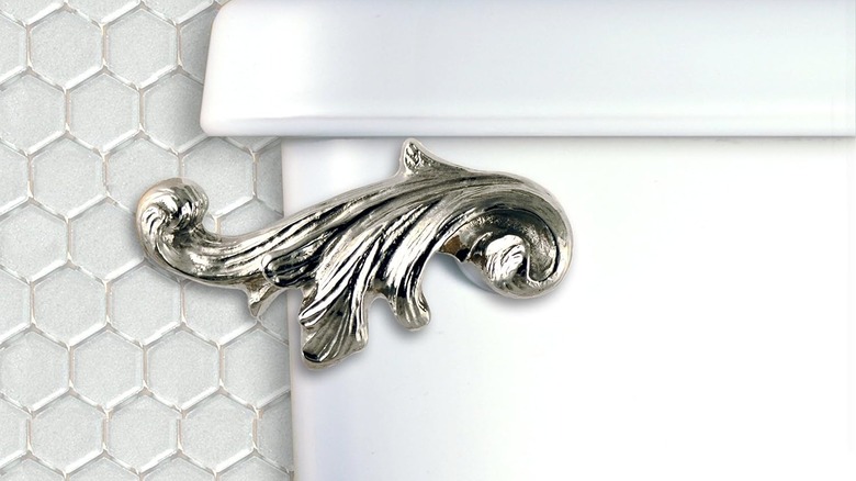 An acanthus leaf toilet flush handle is installed on a white tank