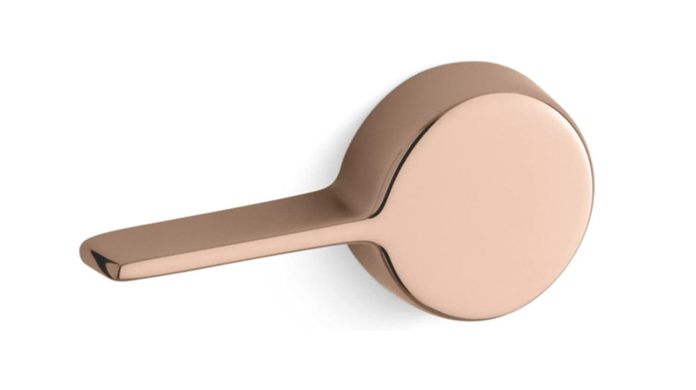 A modern rose gold toilet lever is shown in a detail shot