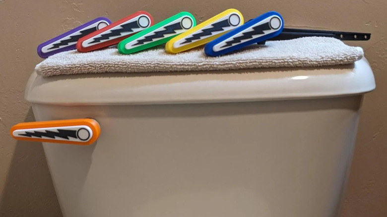 Colorful pinball flapper-inspired toilet flush levers are displayed on a white toilet
