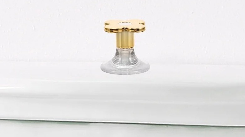 Two gold floral shaped push button toilet flush handles are shown in a detail shot