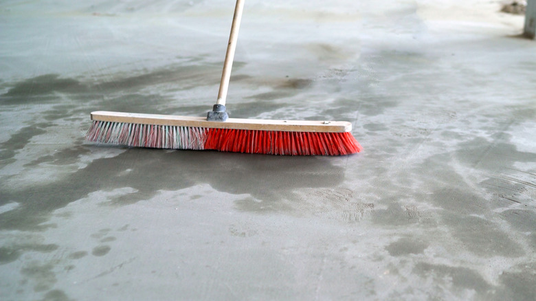 Close-up of a broom sweeping a garage floor with spills