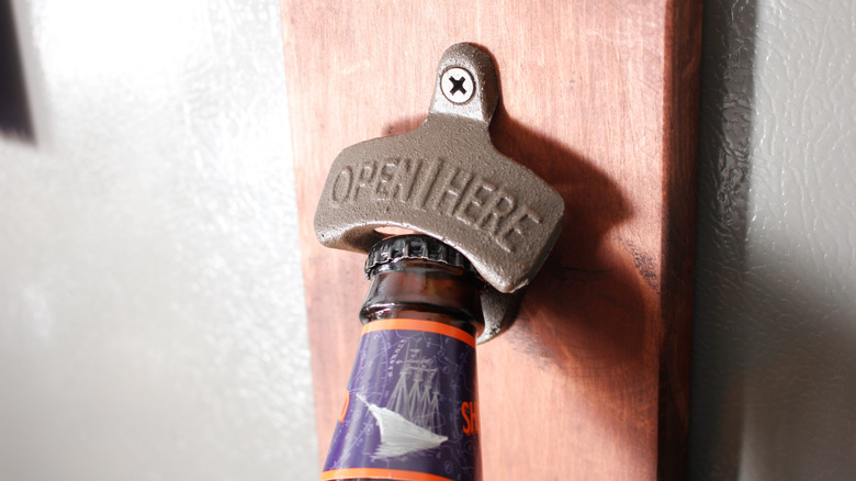 A beer bottle in position underneath a wall-mounted bottle opener