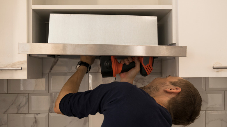 Person installing a range hood in kitchen