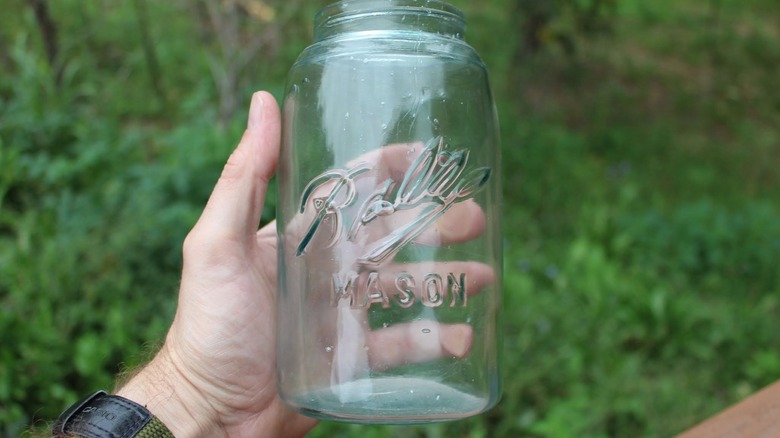 A hand holds a vintage Triple-L Ball jar outside.