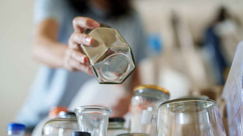 A woman places a glass jar into a collection of glass jars in a plastic tub.