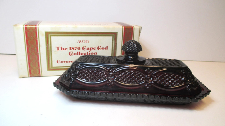 A ruby glass butter dish in front of an Avon box