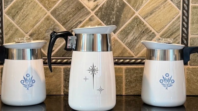 Corningware Starburst and Cornflower Blue percolators on a kitchen counter against a stone backsplash